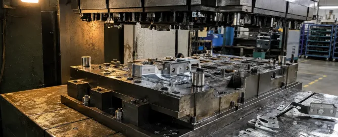 Ein Folgeverbund-Stanzwerkzeug, das während der Tryout-Phase auf einem Hydraulikpressentisch montiert ist, mit Muster-Automobilhalterungsteilen auf der Arbeitsfläche