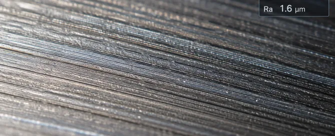 Makro-Nahaufnahme einer bearbeiteten Metalloberfläche mit sichtbaren Werkzeugspuren, Rauheitsspitzen und -tälern, mit einer Overlay-Anzeige der Oberflächenrauheitsmessung